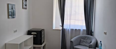 Una habitación pequeña y poco amueblada, con sofá, mesita, televisor y ventana con cortinas.
