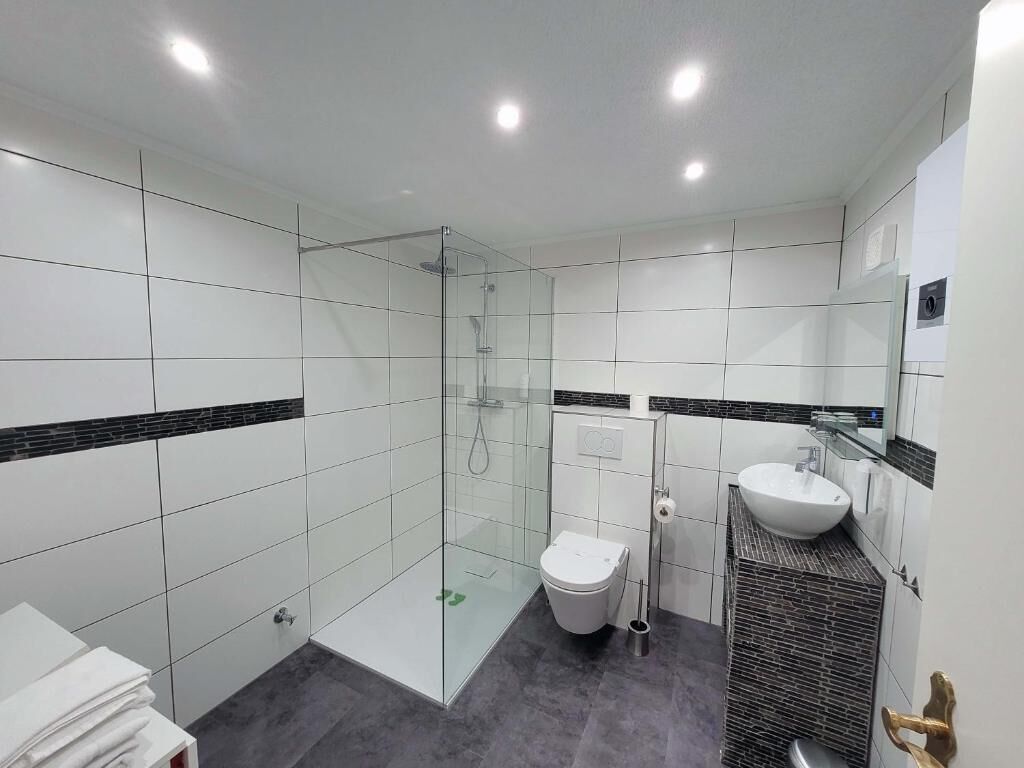 Une salle de bain moderne avec une douche à parois de verre, des toilettes blanches et un lavabo doté d’un plan de travail noir.