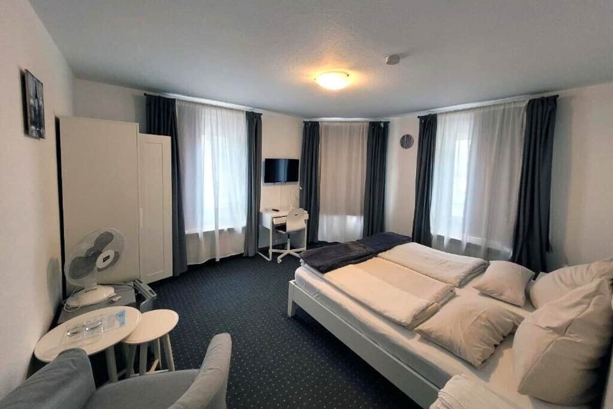 Een hotelkamer met een bed, een bureau, een stoel, een ventilator en gordijnen.