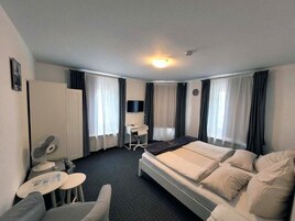 Una habitación de hotel con cama, escritorio, silla, ventilador y cortinas.