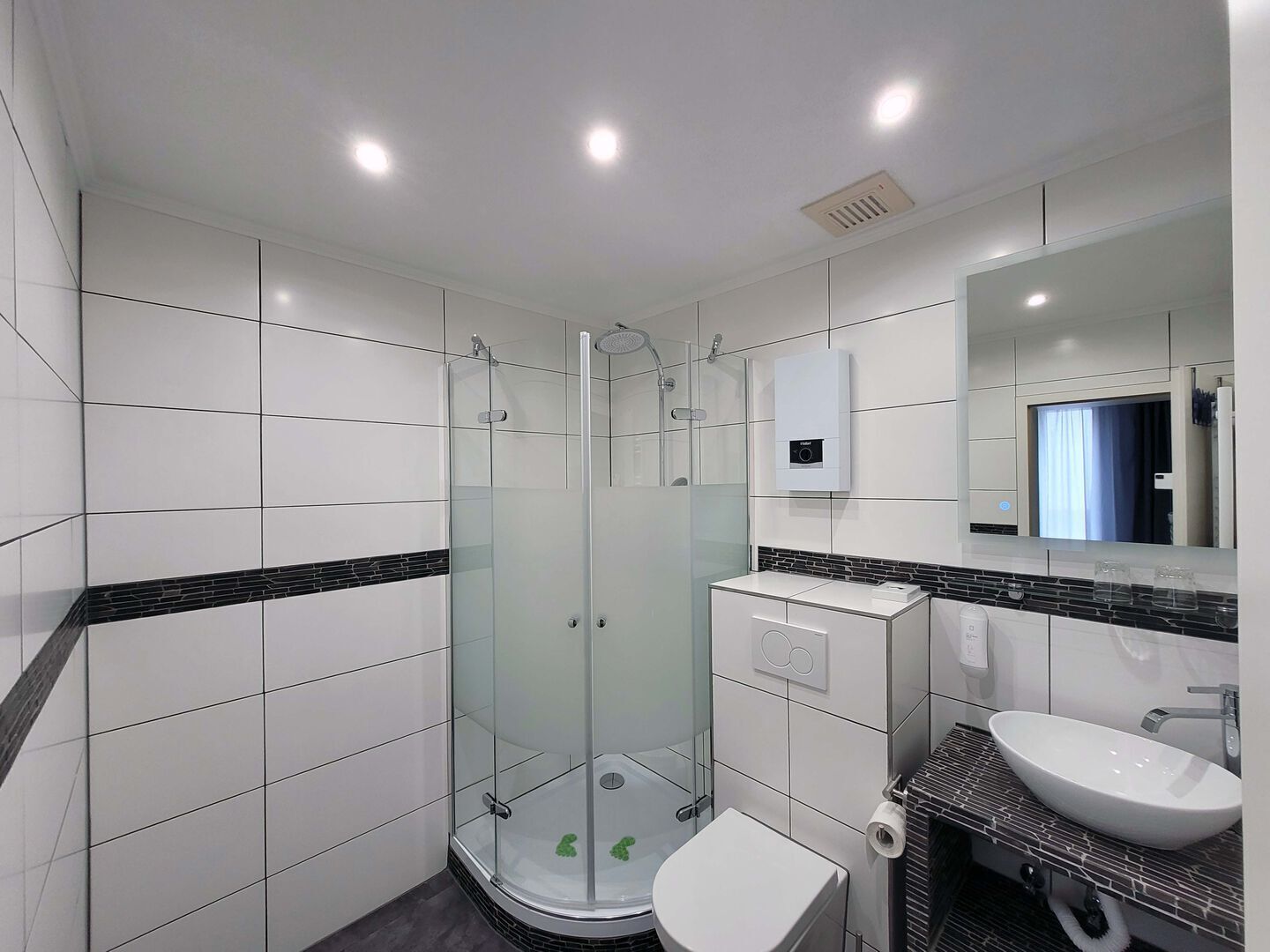 A modern bathroom with a glass-enclosed shower, a white toilet, and a sink with a mirror above it.