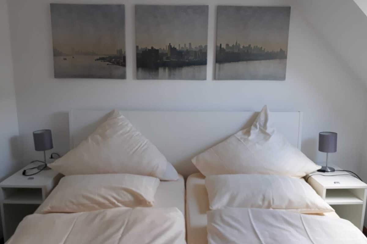 Een hotelkamer met een bed, twee nachtkastjes en drie aan de muur hangende schilderijen van een stadsgezicht.