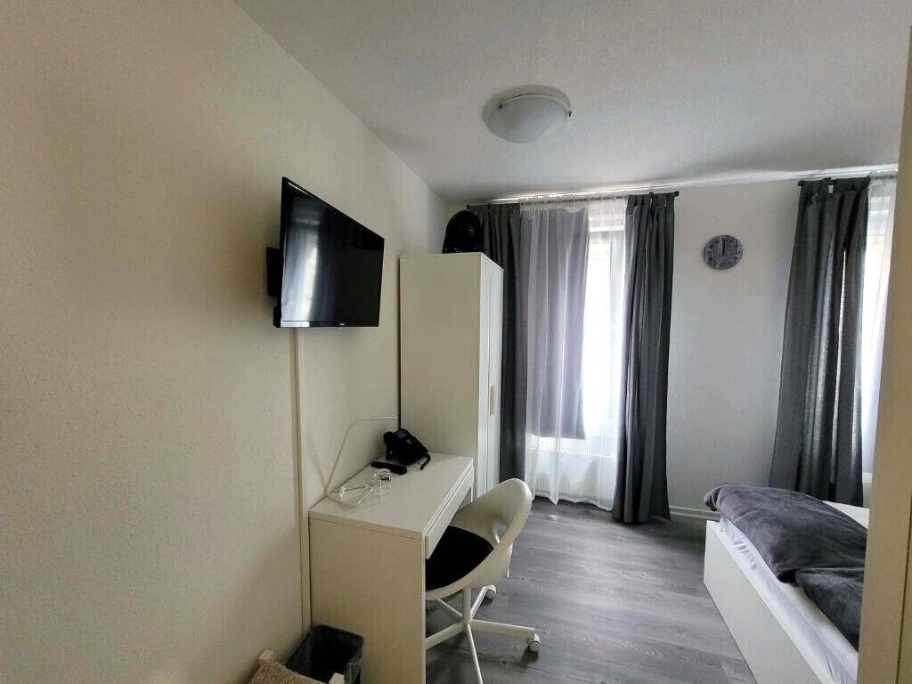 Ein Hotelzimmer mit einem Bett, einem Schreibtisch mit Stuhl, einem an der Wand befestigten Fernseher und einem Fenster mit Vorhängen.