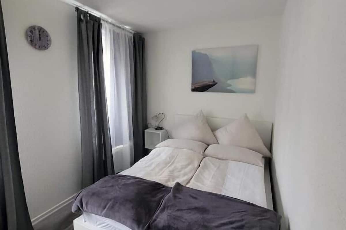 Een slaapkamer met een bed, een nachtkastje, een klok en een schilderij aan de muur.