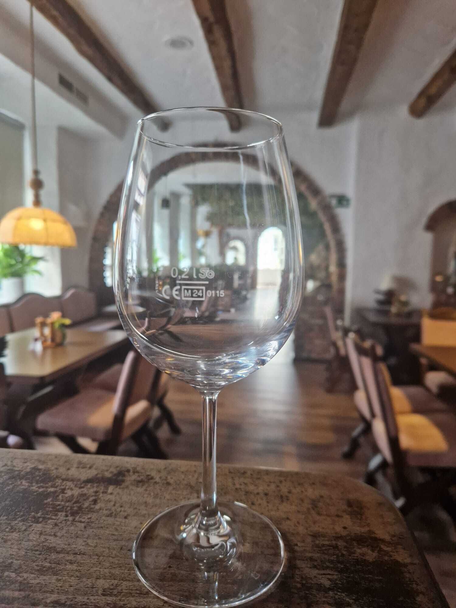 Una copa de cristal transparente con un logotipo visible en el tallo, sobre una mesa de madera en un restaurante con decoración rústica y vigas de madera en el techo.