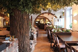 Un restaurante con una decoración rústica, que presenta un gran tronco de árbol, paredes de ladrillo, mesas de madera y un arco de ladrillo que conduce a la zona del bar.