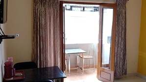 Ein Zimmer mit einem Bett, einem Schreibtisch und einem Stuhl. Es gibt ein Fenster mit Vorhängen und eine Tür, die nach draußen führt.