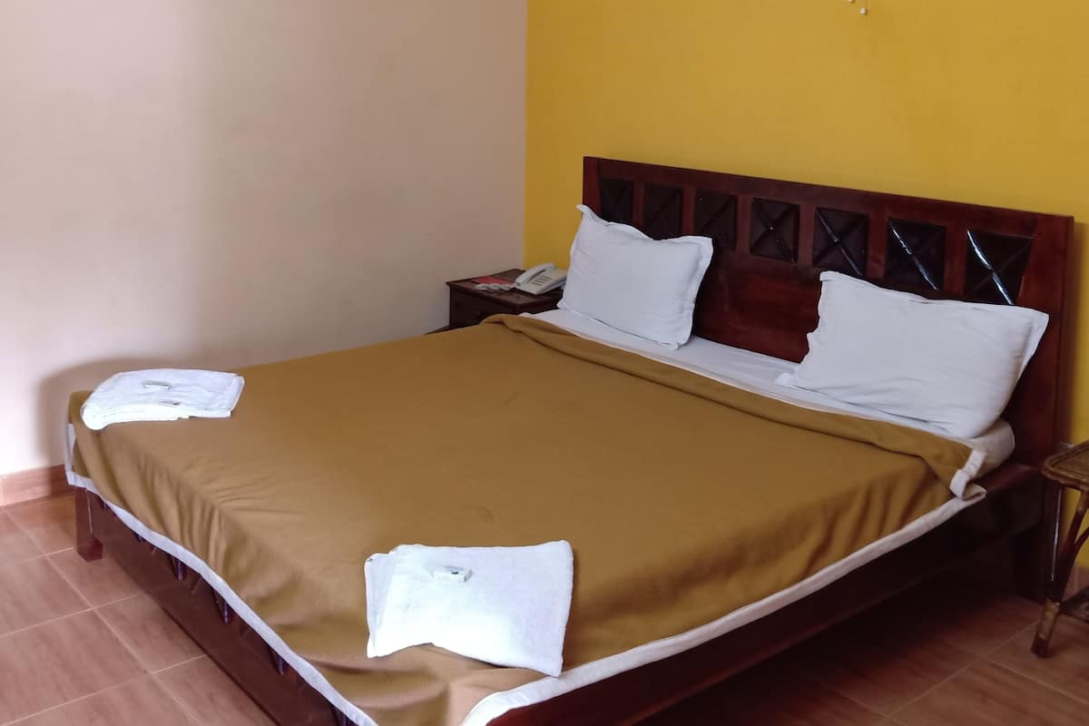 Una habitación de hotel con una cama, una mesita de noche con teléfono y un ventilador de pared.