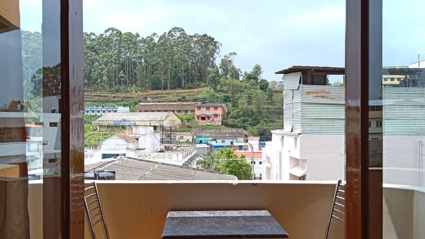 Ein Balkon mit zwei Stühlen und einem Tisch, mit Blick auf eine Wohngegend mit Häusern und Bäumen.