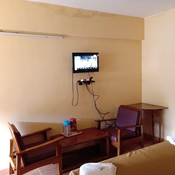 Una habitación pequeña con una televisión en la pared, una mesa de madera, dos sillas y una cama.