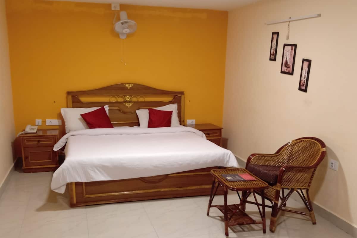 Una habitación de hotel con una cama de madera, ropa de cama blanca, una mesita de noche de madera, una silla de mimbre y una mesita auxiliar.