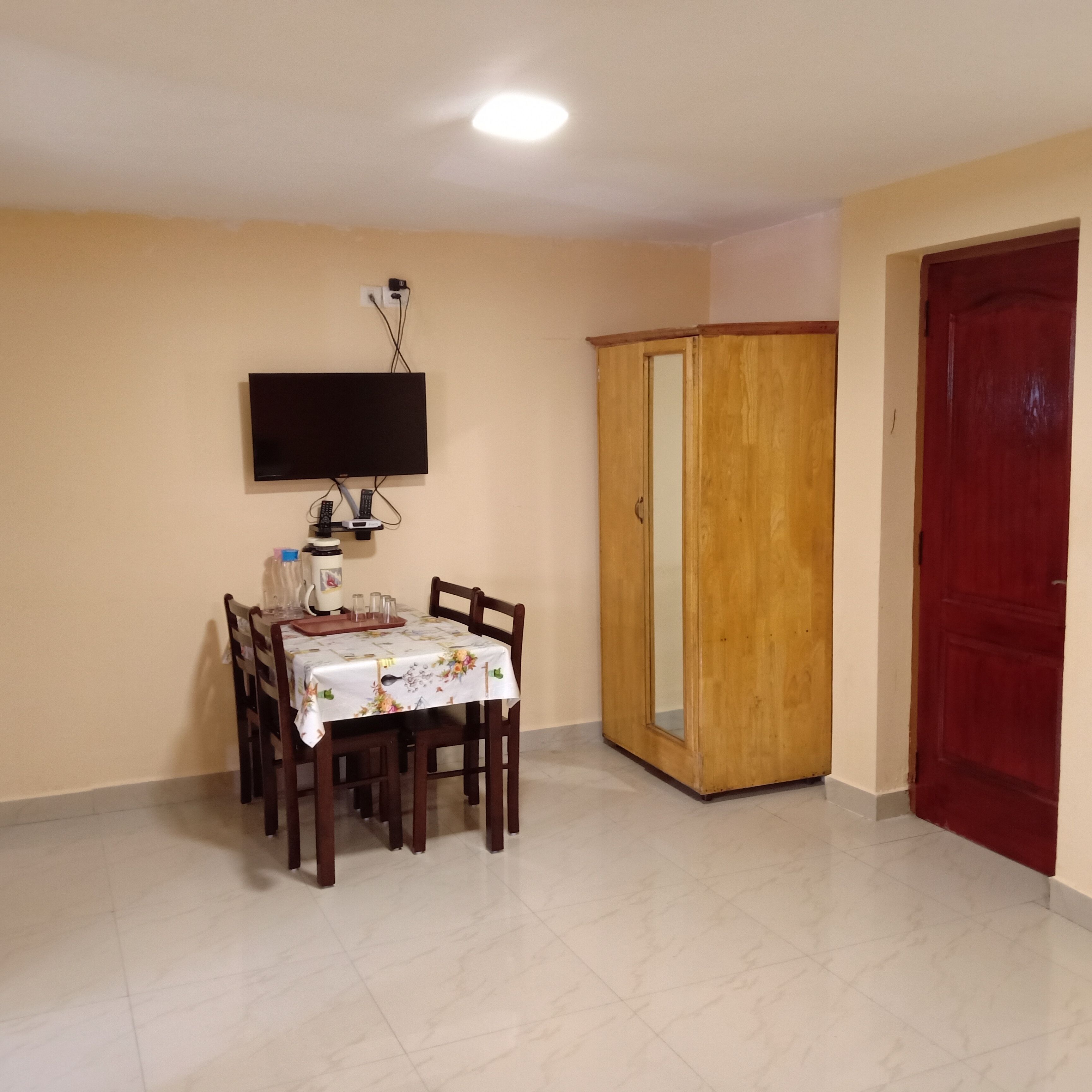 A dining area with a table, chairs, a television mounted on the wall, and a wardrobe.