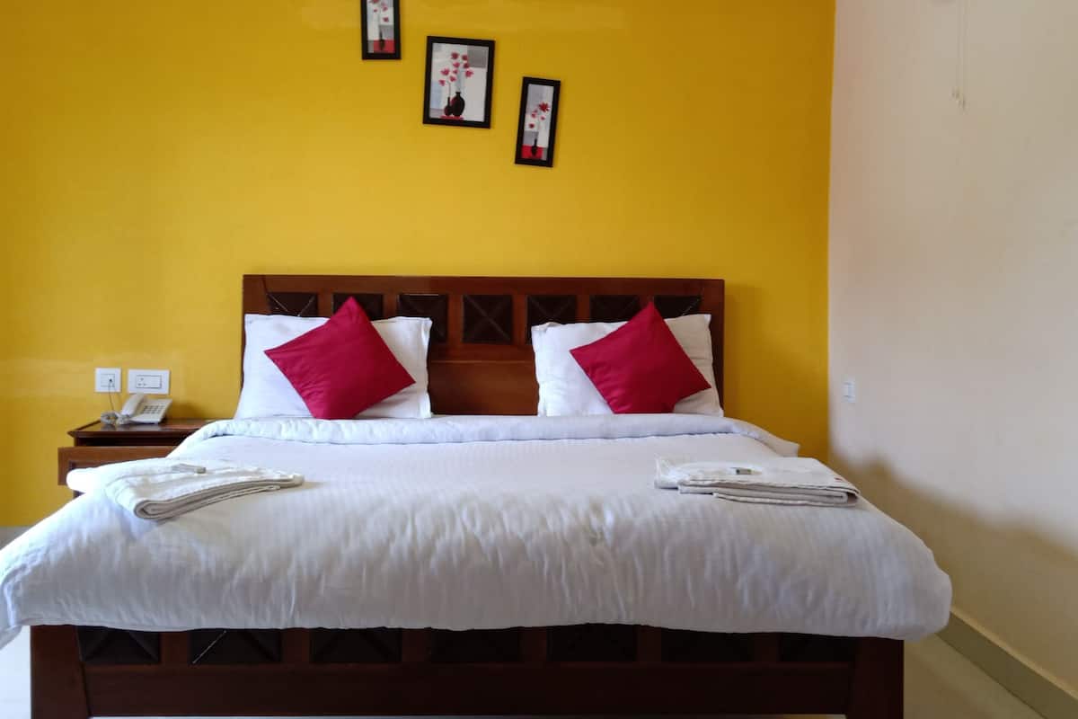 Habitación de hotel con una cama grande, ropa de cama blanca y almohadas rojas. Tres cuadros enmarcados decoran la pared sobre la cama.