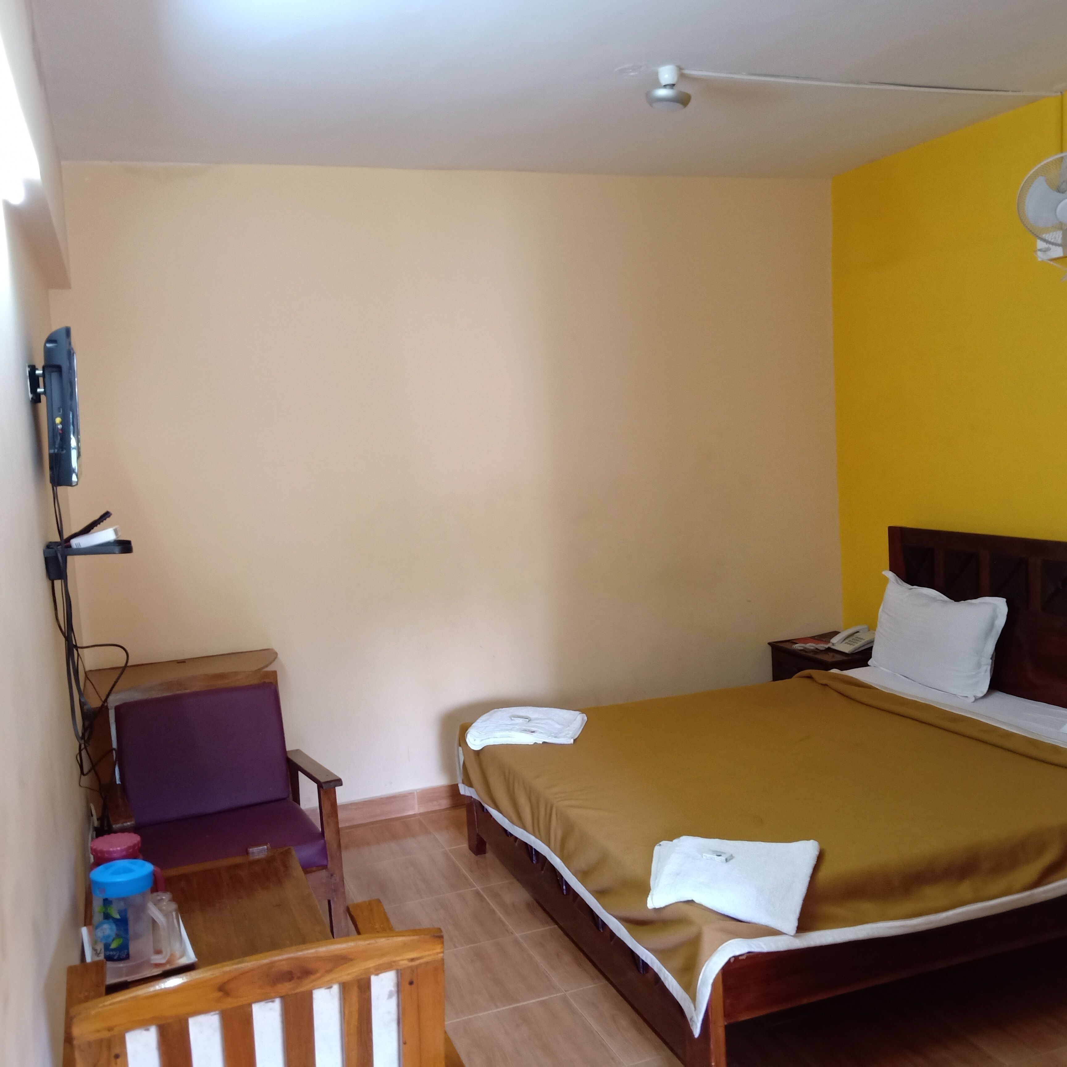 A hotel room with a bed, a desk with a chair, a nightstand, and a wall-mounted phone.