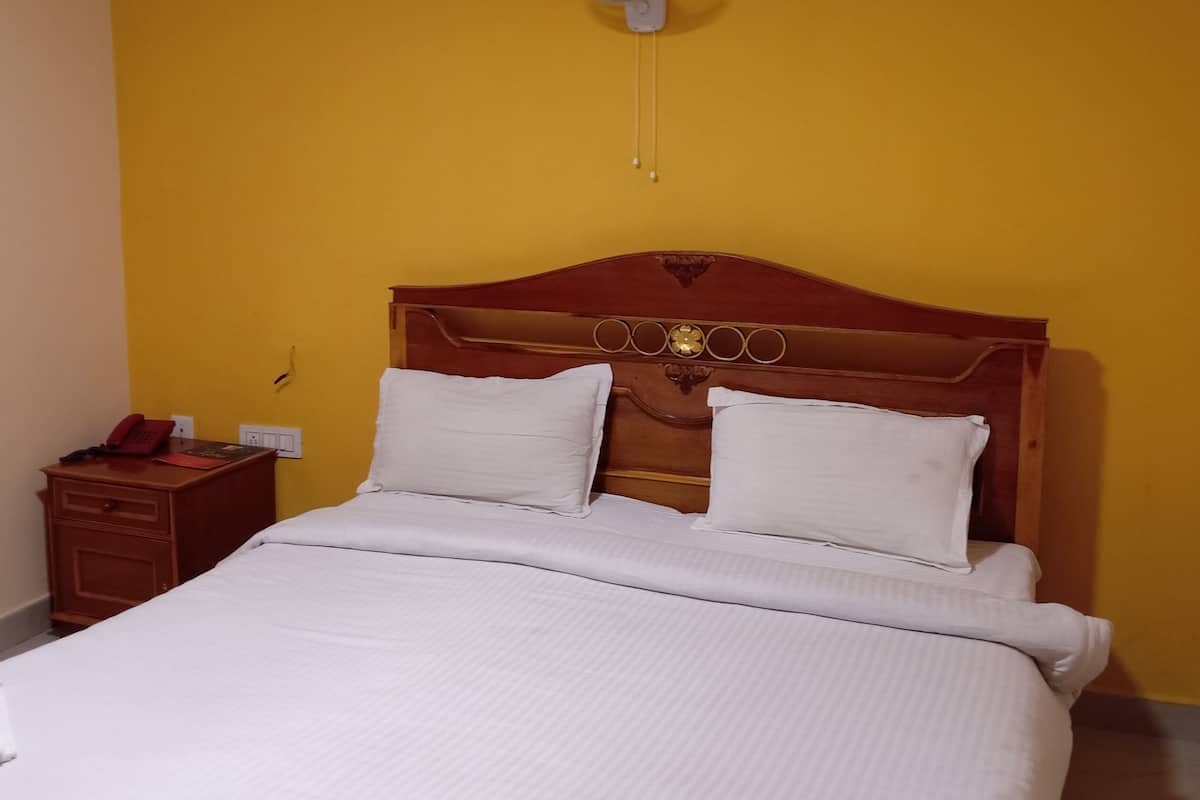 Una habitación de hotel con cabecera de madera, ropa de cama blanca, una mesita de noche con teléfono y un ventilador fijado a la pared.