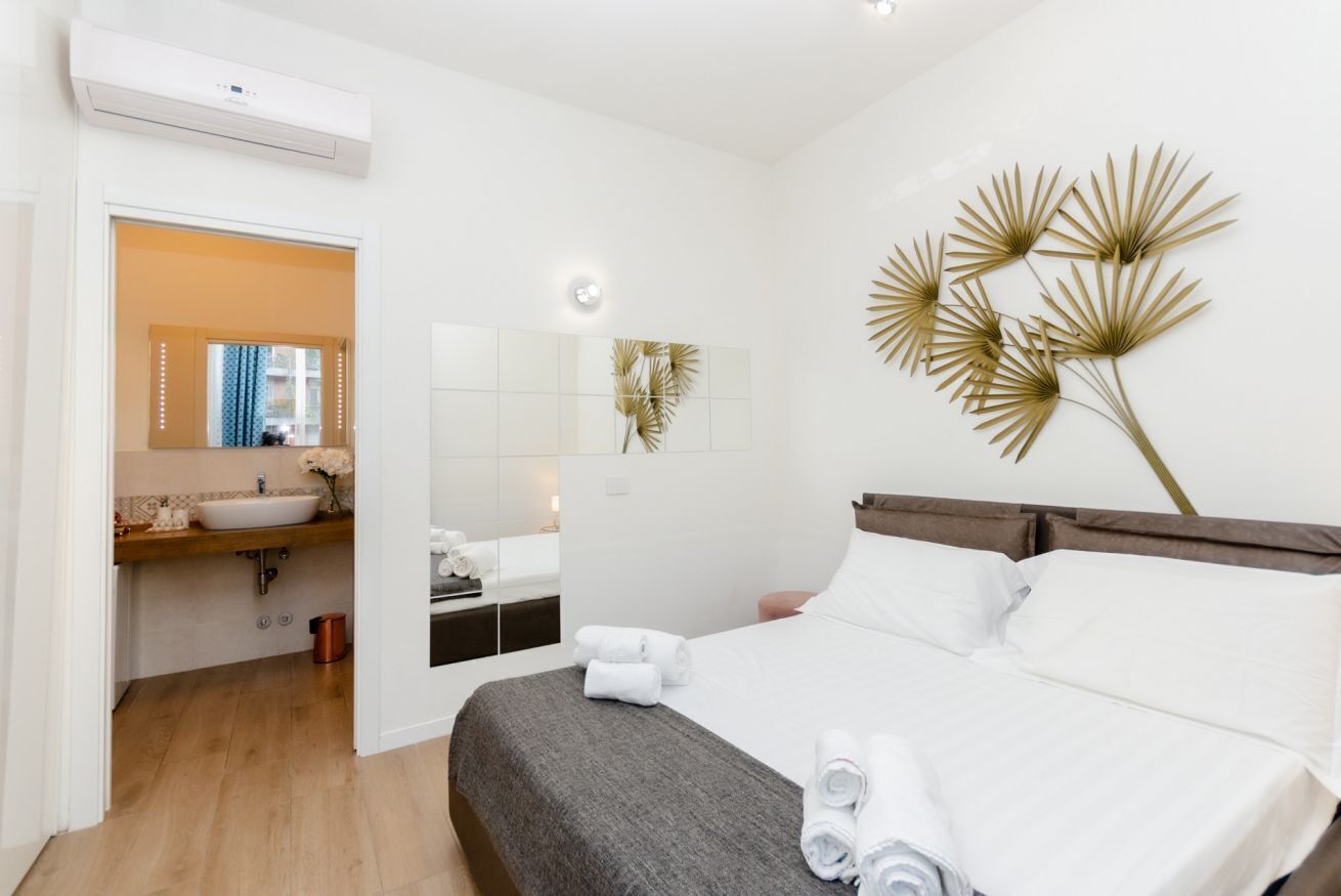 Habitació d'hotel moderna amb un llit gran, una taula de nit, un mirall i una peça decorativa penjada a la paret.
