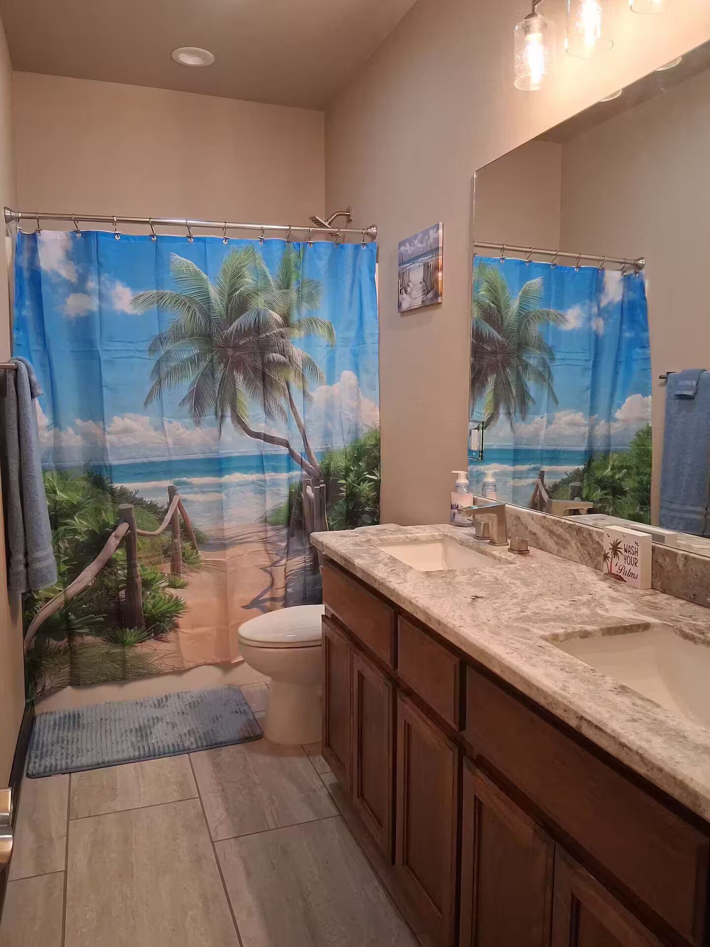 Un baño con cortina de ducha de temática tropical, un lavabo de mármol y armarios de madera.