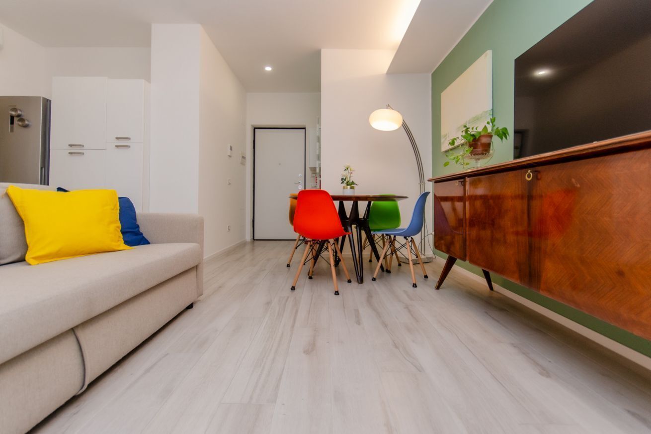 A modern living room with a sofa, colorful chairs, a dining table, and a cabinet.