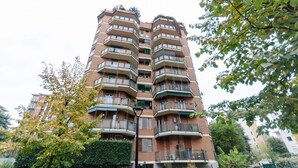 Un immeuble résidentiel à plusieurs étages, doté de balcons, d’une clôture verdoyante et d’arbres.