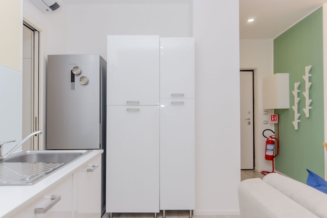 Une cuisine compacte équipée d’un réfrigérateur encastré, d’un évier et d’un meuble blanc.