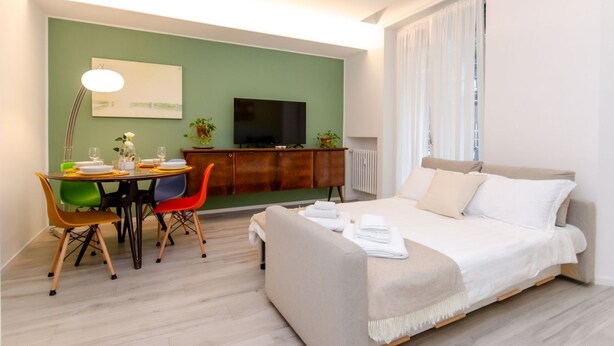 Une chambre d’hôtel moderne équipée d’un lit, d’une table à manger avec des chaises, d’un téléviseur et d’un mur végétal.