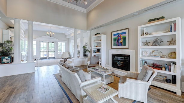 A spacious living room with a fireplace, white furniture, and a bookshelf. - Spacious 7B, 4BA Family Retreat with Game Room & Two Primary Suites! Pool, WIFI, Tennis, Shuttle to the Beach! (Ocean View)