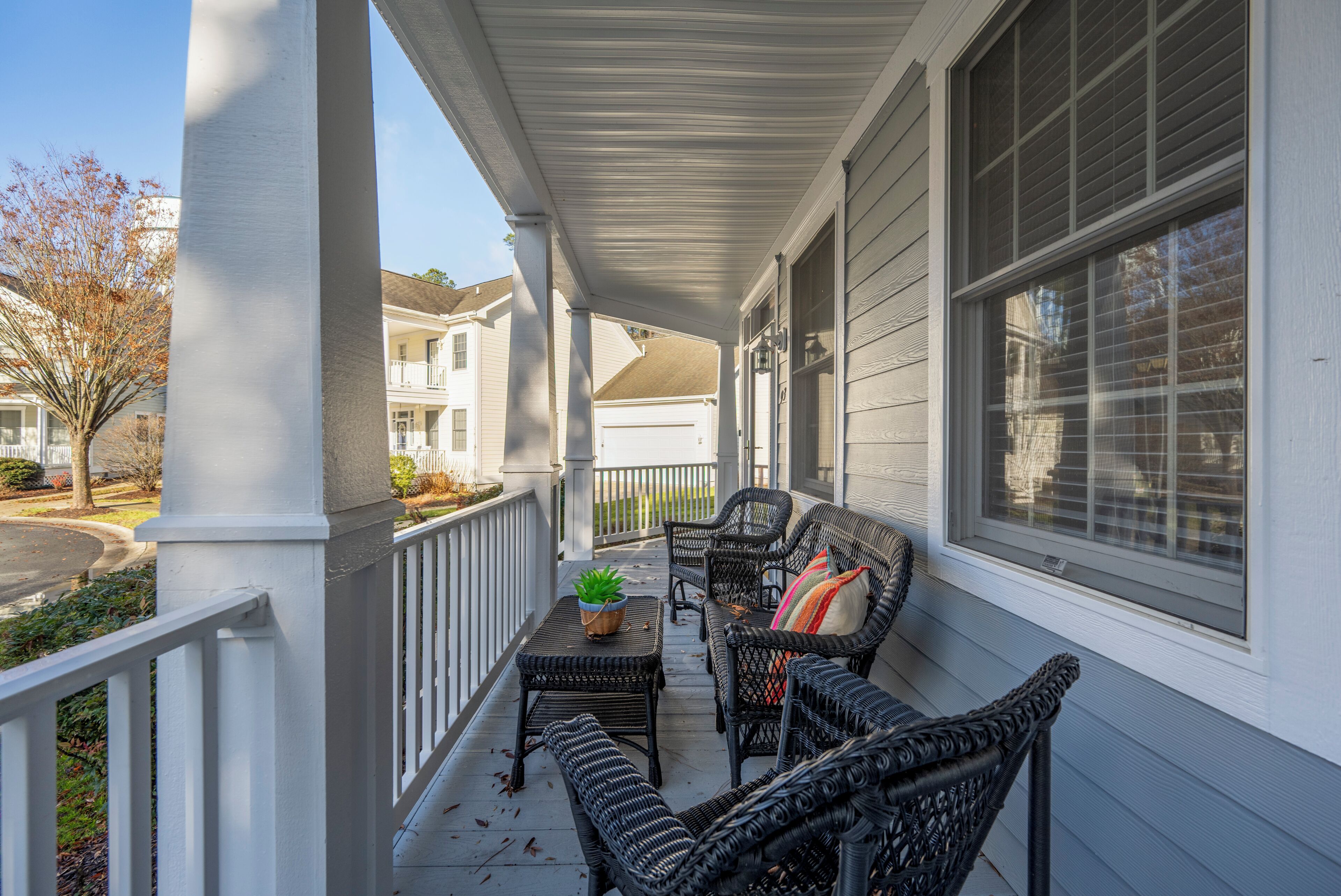 A covered porch with wicker furniture and a potted plant.