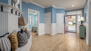 A hallway with a wooden floor, white doors, and a blue wall. There is a bench with pillows and a bag on it. - Spacious 7B, 4BA Family Retreat with Game Room & Two Primary Suites! Pool, WIFI, Tennis, Shuttle to the Beach! (Ocean View)