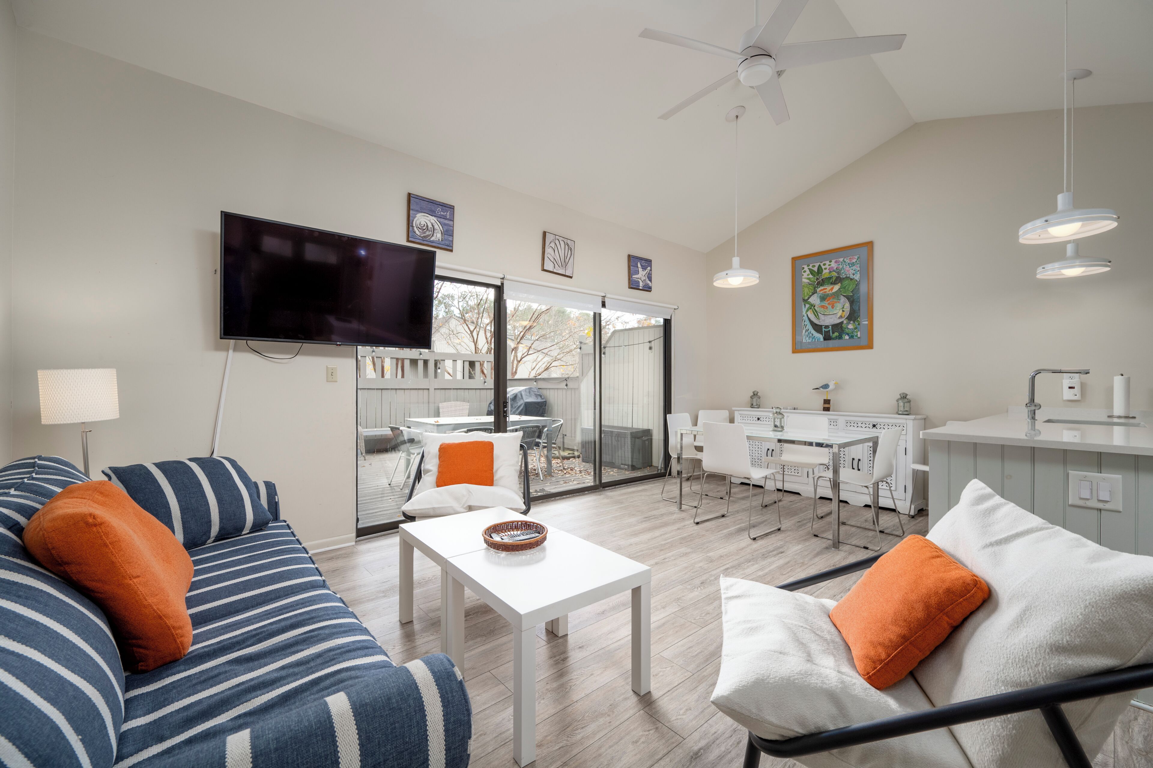 Una sala de estar moderna con un sofá, una mesa de comedor y un televisor. Hay una zona de cocina con una barra y sillas.