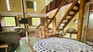 A rustic room with a glass table, a wooden staircase, and a brick wall. - A rustic and charming chalet nestled among centuries-old Jatobá trees! (Piraputanga)
