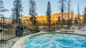 Un bain à remous entouré d’une clôture métallique, avec vue sur une zone boisée.