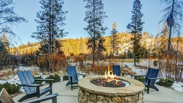 Un foyer en pierre, entouré de fauteuils Adirondack, dans un décor extérieur enneigé, avec une forêt en arrière-plan.