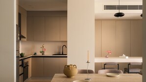 A modern kitchen with a dining area, featuring a wooden table, chairs, and a vase with flowers. - Brassbell Zamalek Diplomatic Zone Near Marriott (Cairo)
