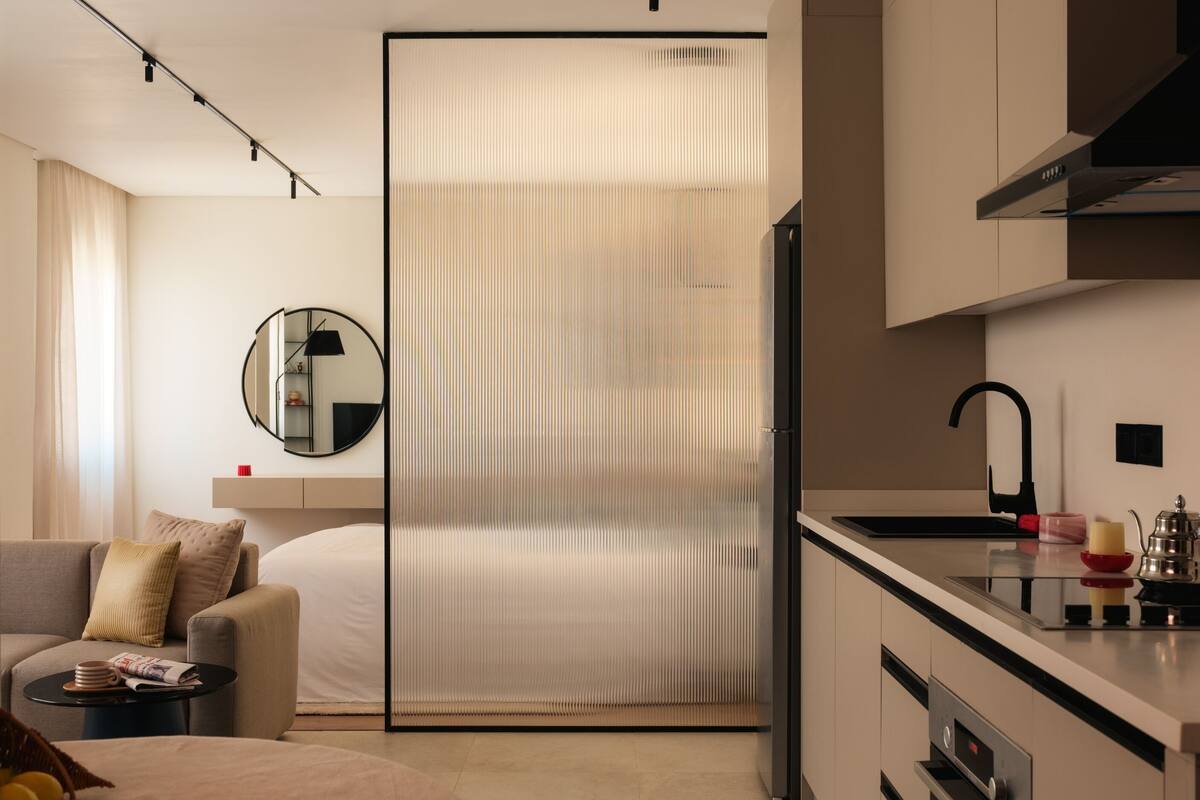 Een moderne hotelkamer met een kitchenette, een bank, een klein tafeltje en een schuifdeur die de woonkamer van de keuken scheidt.