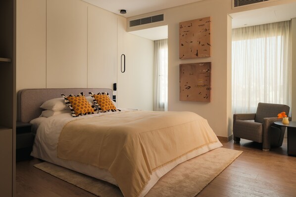 A bedroom with a bed, a chair, a small table, and artwork on the walls. - Brassbell Zamalek Diplomatic Zone Near Marriott (Cairo)