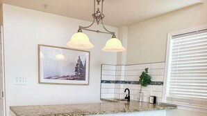 Eine Küche mit einem Zickzack-Muster als Spritzschutz, zwei Barhocker, einer Pendelleuchte und einem gerahmten Bild an der Wand.