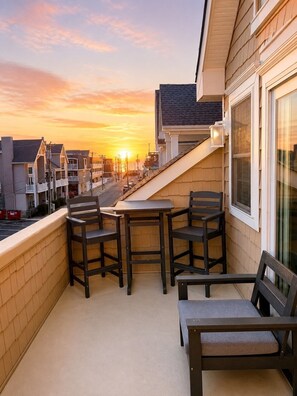 Ein Balkon mit Tisch und Stühlen, der auf eine Straße mit Sonnenuntergang Blick bietet.