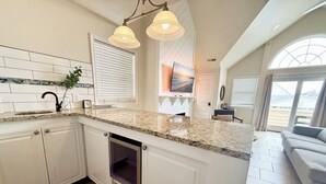 Eine Küche mit weißen Schränken, einer Granit Arbeitsplatte, einem eingebauten Backofen und Pendelleuchten.