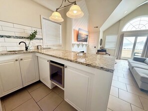 Eine Küche mit weißen Schränken, einer Granit Arbeitsplatte, einem eingebauten Backofen und Pendelleuchten.
