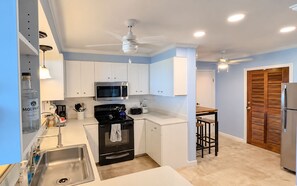 A modern kitchen with white cabinets, a black stove, a microwave, and a refrigerator. - Seachange--views, pool, AC and generator (Christiansted)