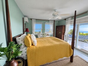 A bedroom with a bed, a ceiling fan, a window with curtains, a potted plant, and a view of the ocean. - Seachange--views, pool, AC and generator (Christiansted)