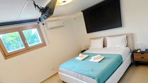 A hotel room with a bed, a nightstand, a TV mounted on the wall, and a window with a view of trees. - Serene,  spacious 4-bedroom villa in beautiful Pelion, located on the west side (Artemis)