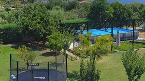A trampoline surrounded by a safety net, with a pool and a view of the sea in the background. - Serene,  spacious 4-bedroom villa in beautiful Pelion, located on the west side (Artemis)
