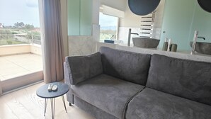 A modern living room with a grey sofa, a small round table, and a view of the outdoors through a large window. - Serene,  spacious 4-bedroom villa in beautiful Pelion, located on the west side (Artemis)