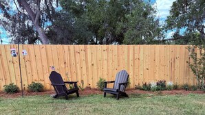 Un jardin avec deux fauteuils Adirondack, une clôture en bois et une nichoir.