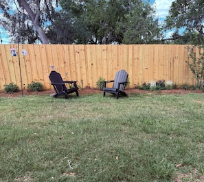 A backyard with two Adirondack chairs, a wooden fence, and a birdhouse. - Stylish 2BR in Ocala Near WEC & FAST (Ocala)