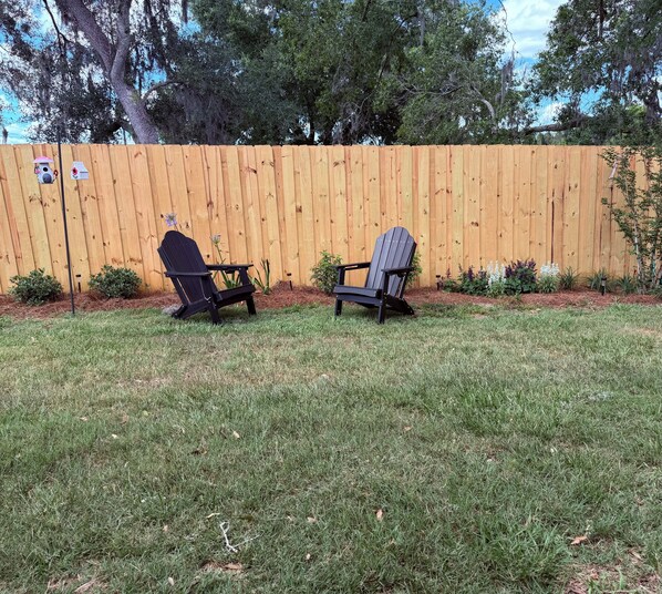 A backyard with two Adirondack chairs, a wooden fence, and a birdhouse.