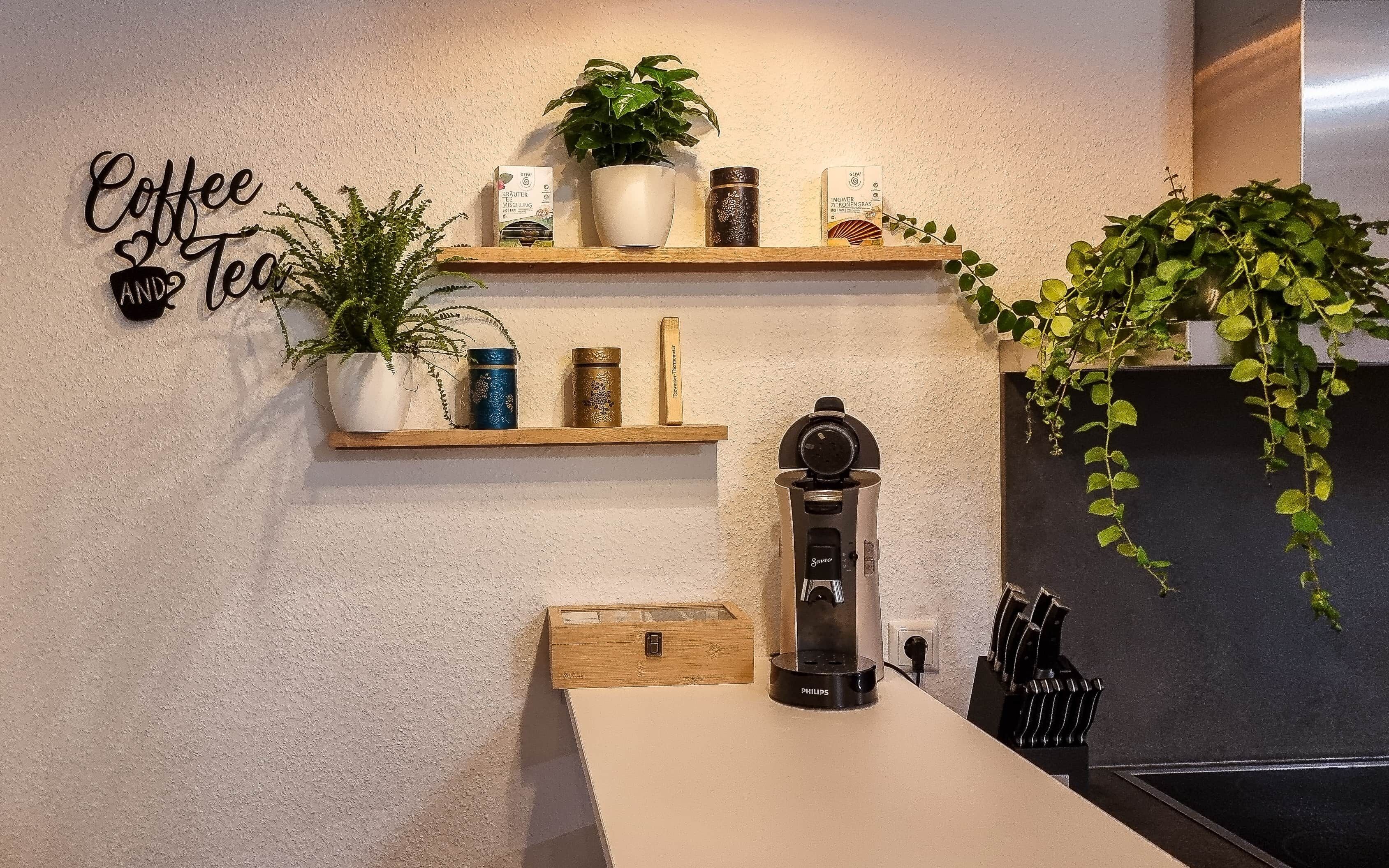 Eine Küche mit Schild für Kaffee und Tee, einer Kaffeemaschine und verschiedenen Pflanzen auf Regalen.