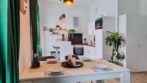 Moderni keittiö, jossa on valkoiset kaapit, sisäänrakennettu uuni ja mikroaaltouuni. Ruokapöytä on katettu lautasilla, aterimilla ja kynttilällä.