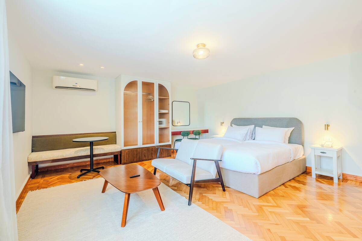 Una habitación de hotel con cama, sofá, mesita, banco y armario.